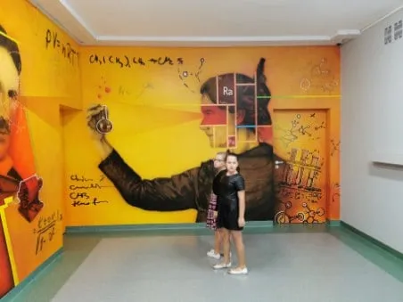 Mural z Marią Skłodowską-Curie i symbolem radu, przed nim dwie uczennice